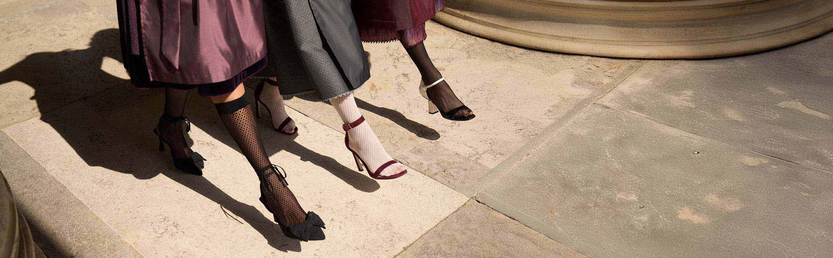 Stylishe High Heels und gemusterte Strümpfe – FALKE X Kinga Mathe Drei Frauenbeine in eleganten High Heels mit gemusterten Strümpfen auf hellem Steinboden – Fashion-Kollaboration FALKE X Kinga MatheDrei Frauenbeine in eleganten High Heels mit gemusterten Strümpfen auf hellem Steinboden – Fashion-Kollaboration FALKE X Kinga Mathe