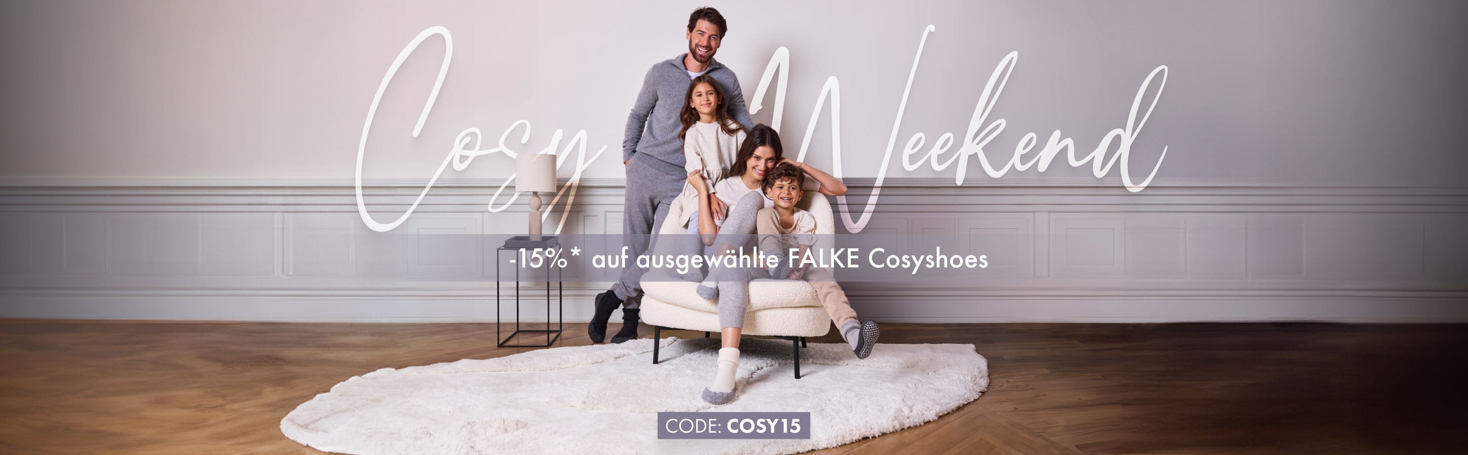 Familie in gemütlicher Loungekleidung von FALKE sitzt lachend auf einem Sessel. Werbung für „Cosy Weekend“ mit 15 % Rabatt auf ausgewählte FALKE Cosyshoes.