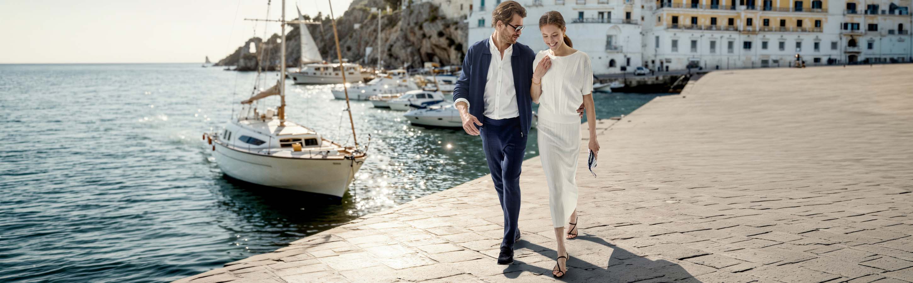 Ein Paar läuft an einem Bootssteg entlang, sie tragen Bekleidung von FALKE.