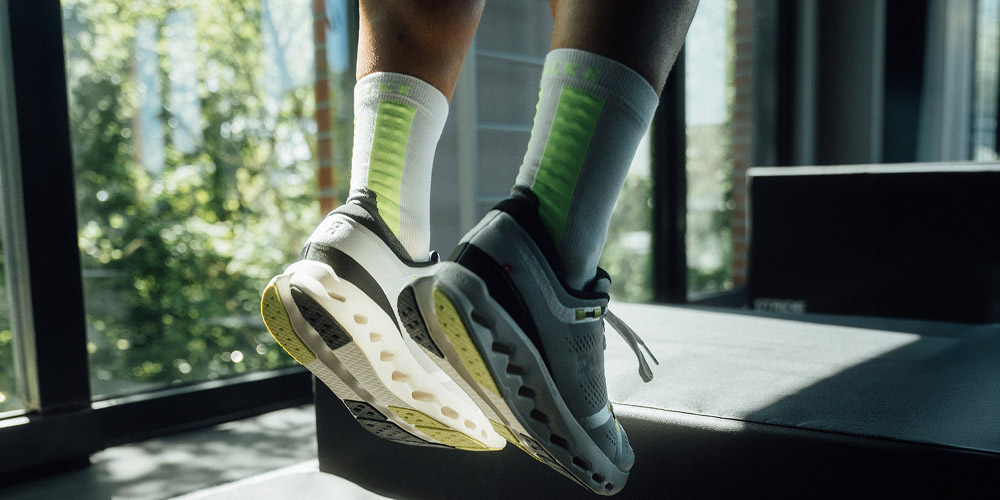 Close-up van witte hardloopsokken met groene details en sneakers op een trainingsbank.