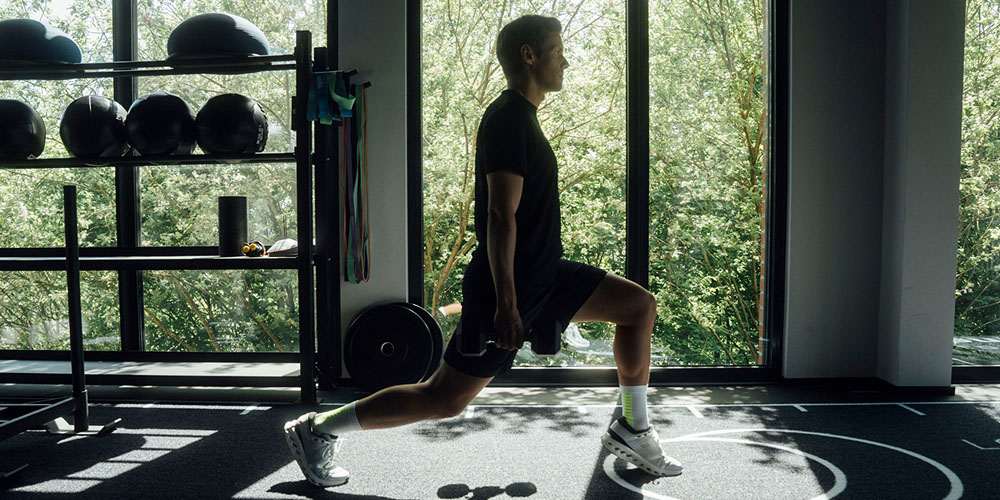 Man maakt een uitvalspas in de fitnessruimte en draagt witte hardloopsokken met groene details en sneakers.