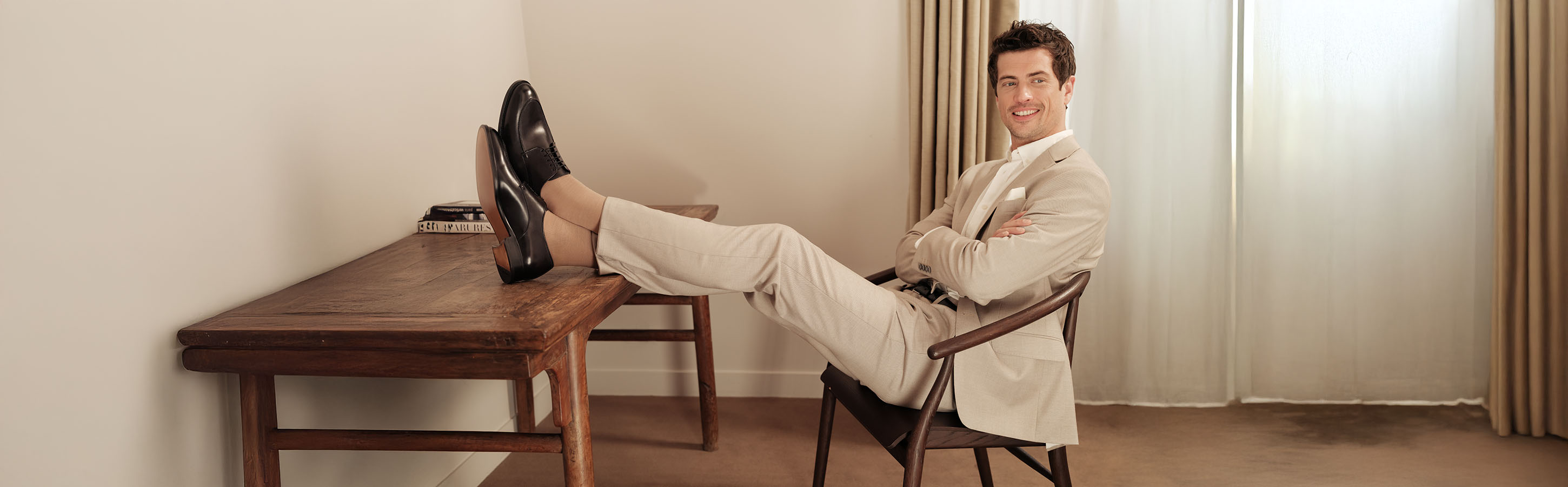 Mann trägt beige Socken der Serie Airport von FALKE, sitzt auf einem Stuhl und hat die Beine auf den gegenüberstehenden Tisch gelegt