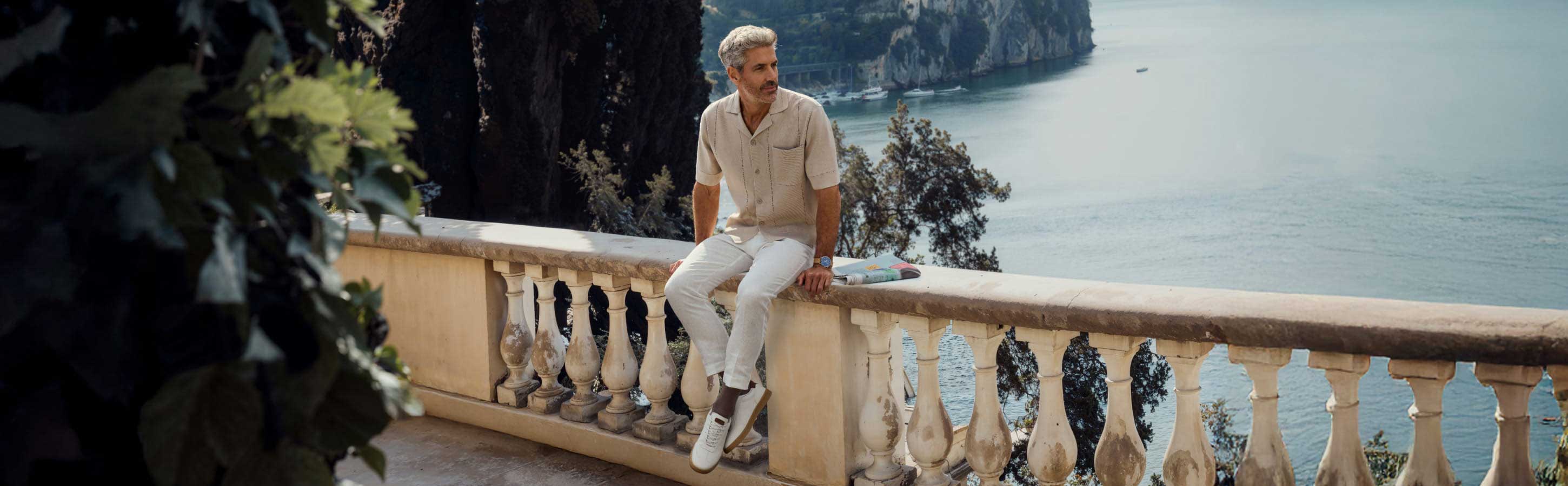 Mann trägt braune Socken der Serie Tiago von Falke und sitzt auf einer Brüstung oberhalb vom Meer