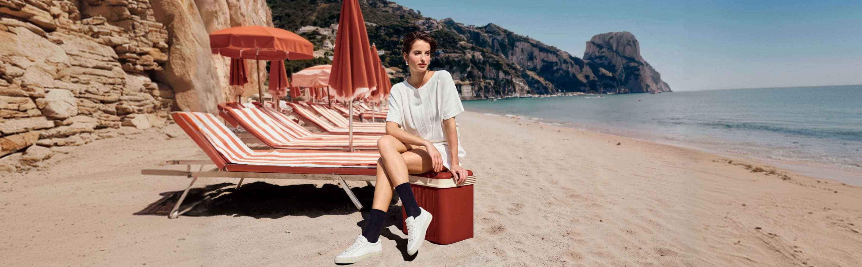 Frau sitzt am Strand auf einer Liege und trägt dunkle FALKE Family Socken zu weißen Sneakern und einem leichten Sommeroutfit