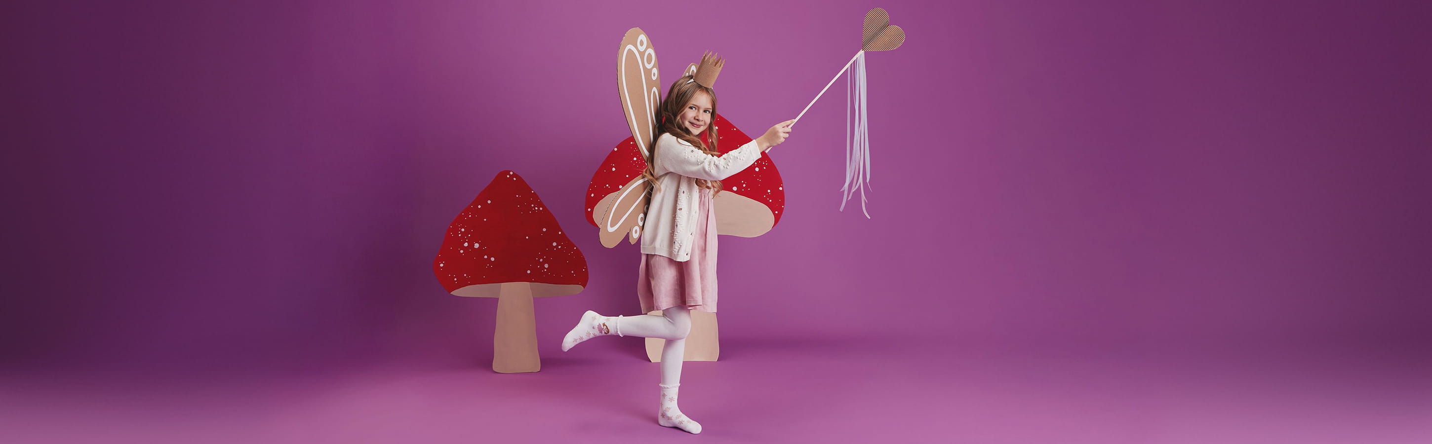 FALKE Fairy Kinder Socken Mädchen im Feenkostüm trägt weiße FALKE Socken mit verspieltem Muster vor einer fantasievollen Pilzkulisse