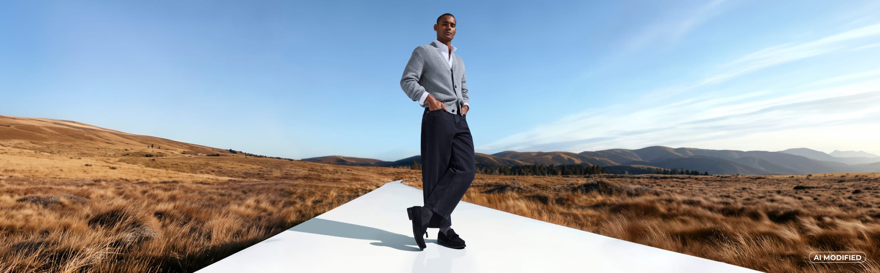 Mann trägt schwarze Hose, einen grauen Strickcardigan und dazu gemusterte Socken der Serie Family Special von FALKE und steht auf einem Laufsteg auf einer Wiese Mann in grauer Strickjacke und dunkler Hose mit dunklen Socken in herbstlicher Landschaft. Das Bild ist KI modifiziert.