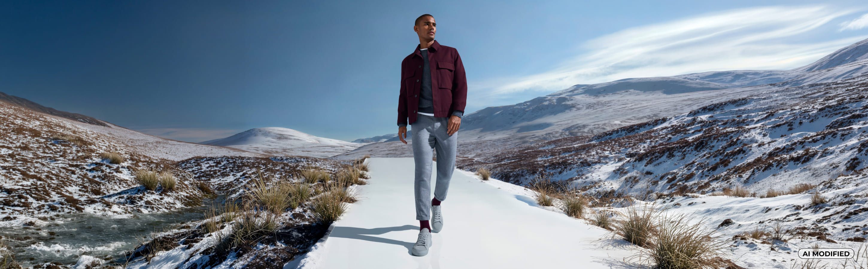 Mann trägt graue, eine dunkelrote Jacke und dazu dunkelrote Socken der Serie Lhasa Rib von FALKE und steht auf einem Laufsteg zwischen einer schneebedeckten Wiese