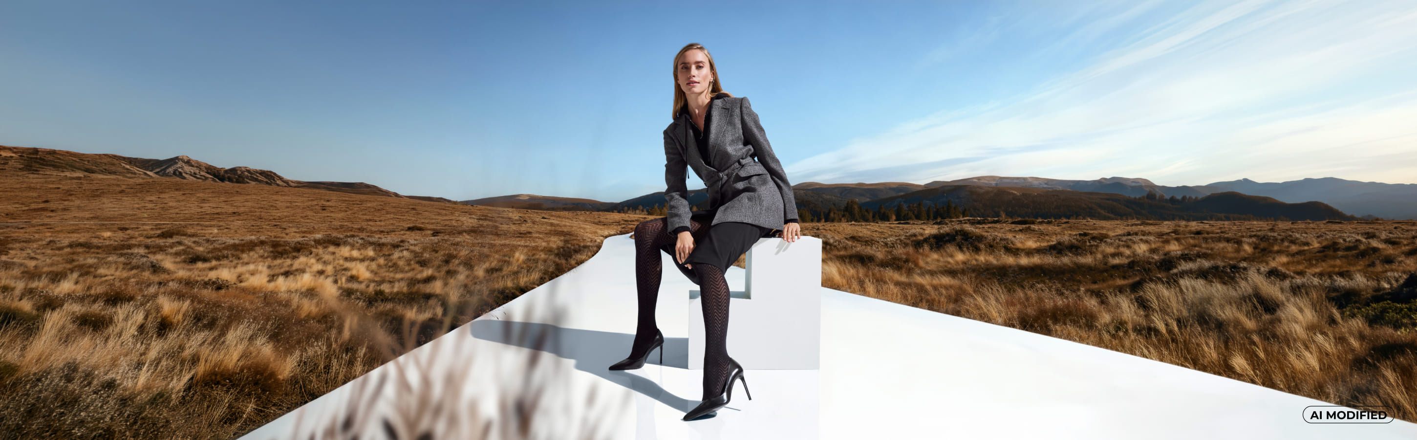 Frau im grauen Blazer mit dunkel gemusterter Strumpfhose sitzt in herbstlicher Landschaft. Das Bild ist KI modifiziert.